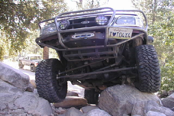 Red Ford Ranger with custom roll cage and winch, front view, on rocks