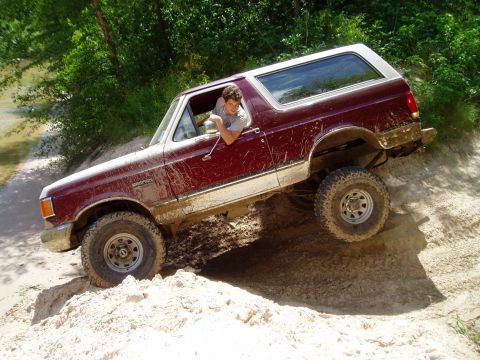 1990 Ford Bronco - A maroon 1990 Ford Bronco navigates a challenging sandy incline during an off-road excursion.