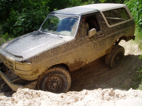1990 Ford Bronco - A heavily muddied 1987 Ford Bronco is stuck off-road, its tires digging into the sand.