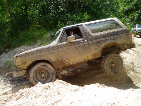 1990 Ford Bronco - Muddy 1990 Ford Bronco tackling an off-road trail; another vehicle is seen behind it.