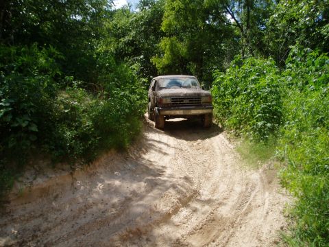 1990 Ford Bronco - A dusty Ford Bronco navigates a muddy, overgrown trail.