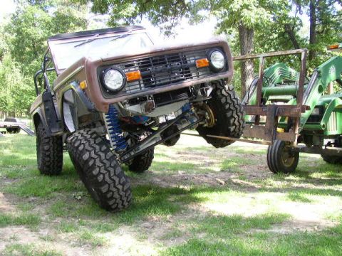 1995 Ford Bronco - A Ford Bronco is being lifted by a tractor loader in a grassy, wooded area.