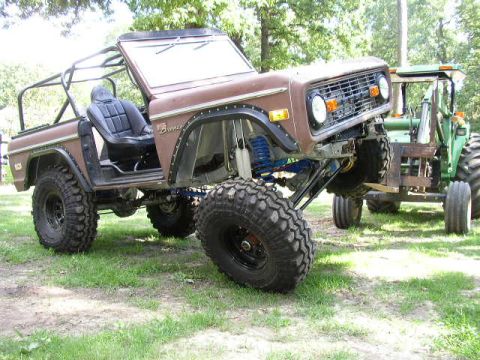 1995 Ford Bronco - This heavily modified Ford Bronco sits high off the ground, with a tractor visible behind it.
