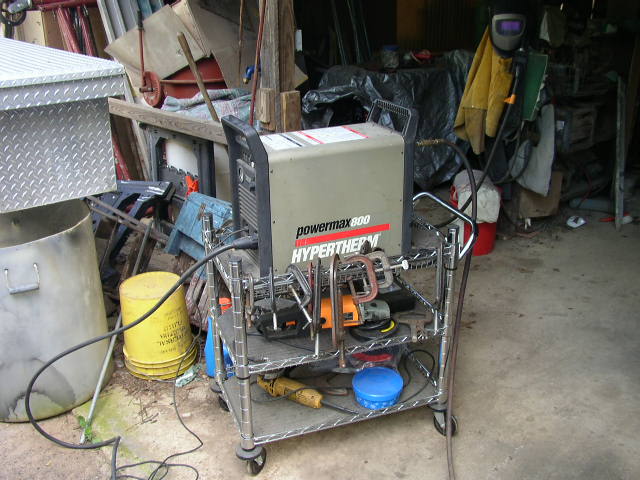 Welding machine on a cart with tools and a yellow bucket nearby in a cluttered garage
