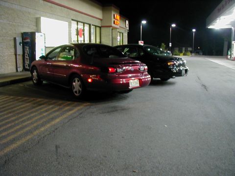 1997 Ford Taurus - Two sedans are parked at a gas station at night, one red and one black.