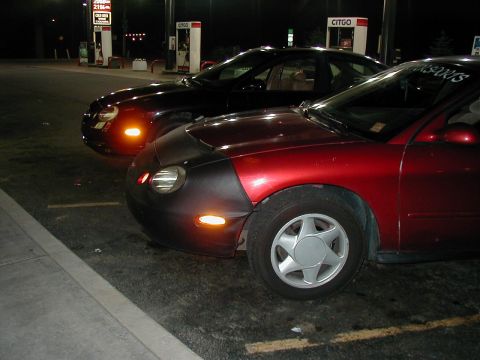 1997 Ford Taurus - Two cars, a red 1997 Ford Taurus and a black car, are parked at a gas station at night.