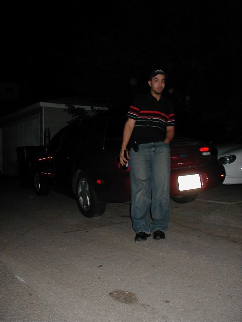 1997 Ford Taurus - A man stands next to a red car at night, with another vehicle partially visible in the background.