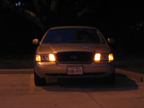 2000 Ford Crown Victoria - A gold Ford Crown Victoria is parked outside at night with its headlights illuminated.