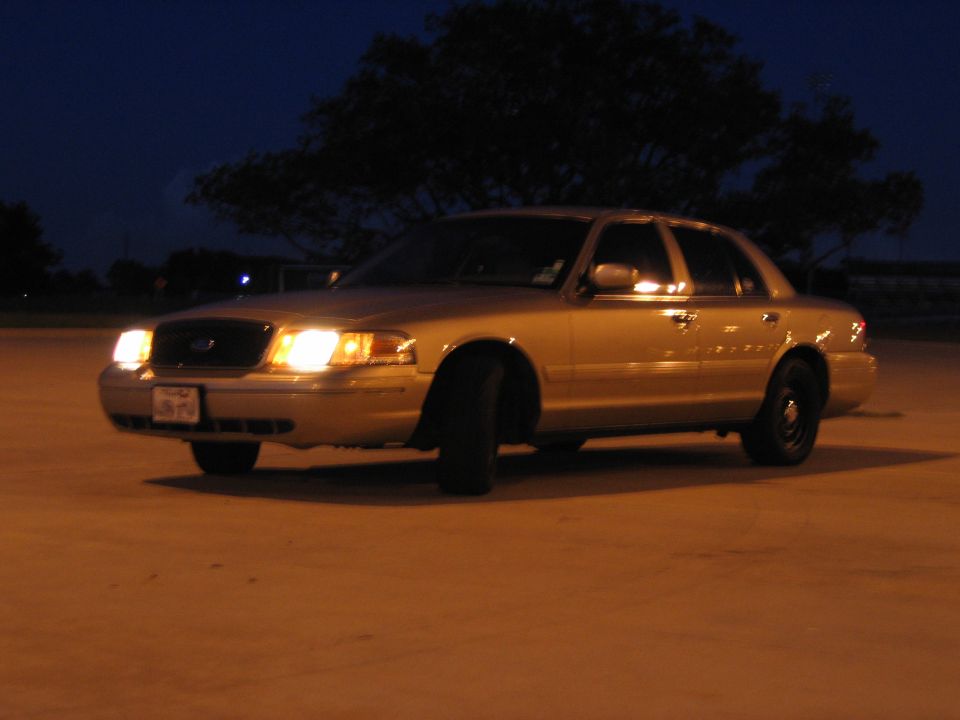 Gold 2000 Ford Crown Victoria sedan parked on concrete at night, front passenger side visible