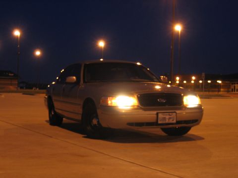 2000 Ford Crown Victoria - A silver 2000 Ford Crown Victoria is parked under streetlights at night, its headlights illuminated.