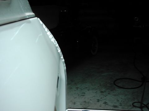 1978 Ford Bronco - Close-up of a damaged white vehicle fender, with another vehicle partially visible in the dark background.