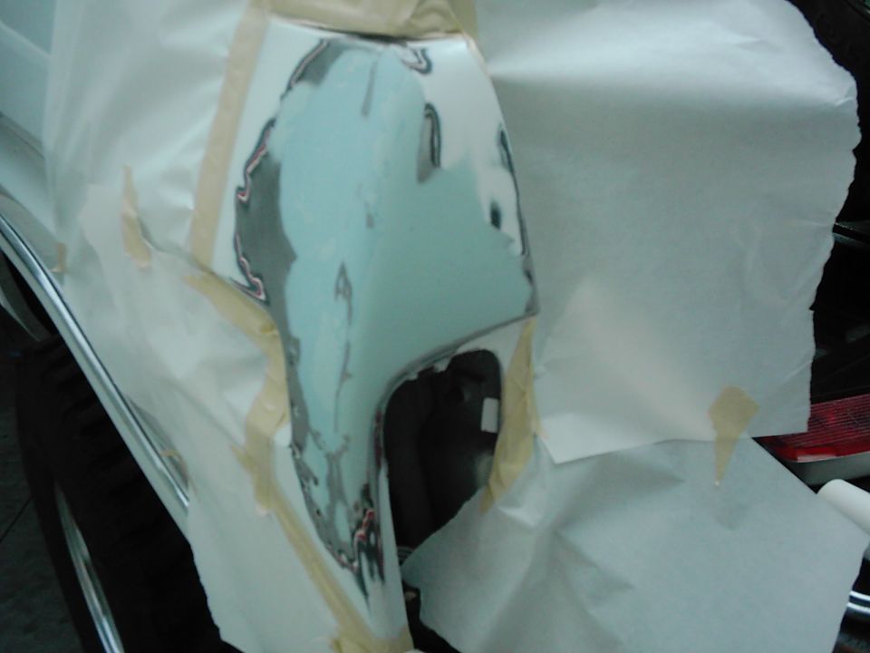 Car fender being repaired with body filler, covered in masking paper and tape