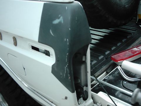 1978 Ford Bronco - This white vehicle's rear quarter panel is undergoing repair, with primer and filler visible on the damaged area.