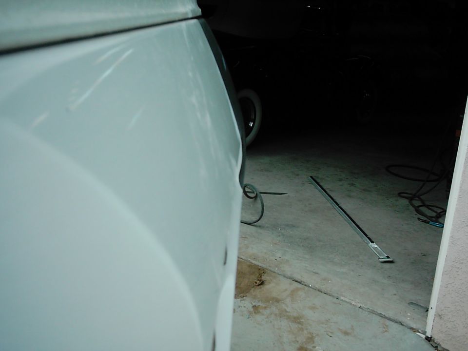 Close-up of a white vehicle panel with a dark garage interior in the background. A metal trim piece lies on the floor