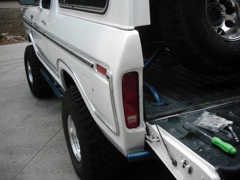 1978 Ford Bronco - The rear of a white 1978 Ford Bronco is visible, with its tailgate down and a spare tire and tools inside.