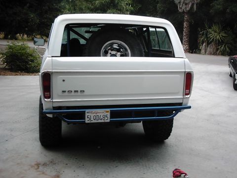1978 Ford Bronco - Rear view of a white 1978 Ford Bronco with a blue roll cage and spare tire visible through the rear window.