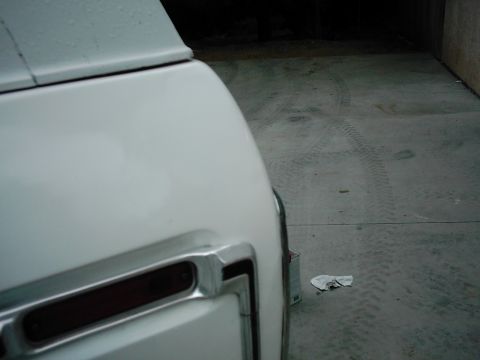 1978 Ford Bronco - A partial view of a white vehicle's rear corner, with tire marks visible on the concrete ground.