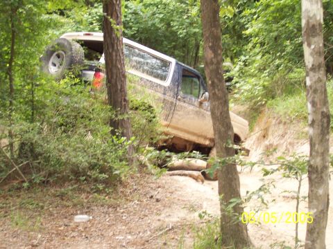 1987 Ford Bronco - A 1987 Ford Bronco navigates a challenging off-road trail, its tires kicking up dirt.