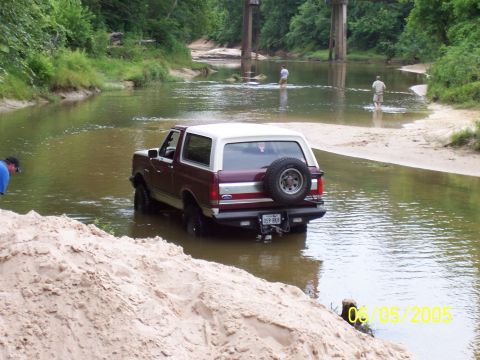 1987 Ford Bronco - A 1987 Ford Bronco navigates a shallow river crossing under a bridge.