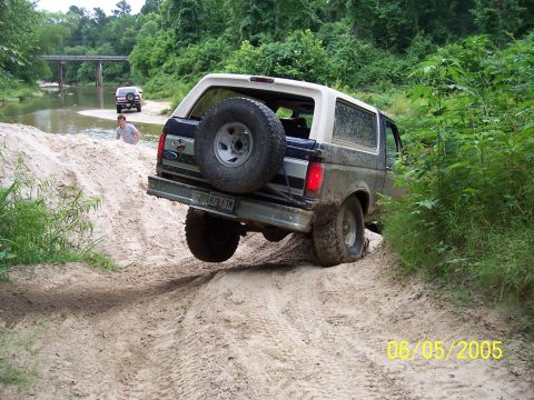 1987 Ford Bronco - A 1987 Ford Bronco navigates a sandy trail near a creek with another vehicle visible.