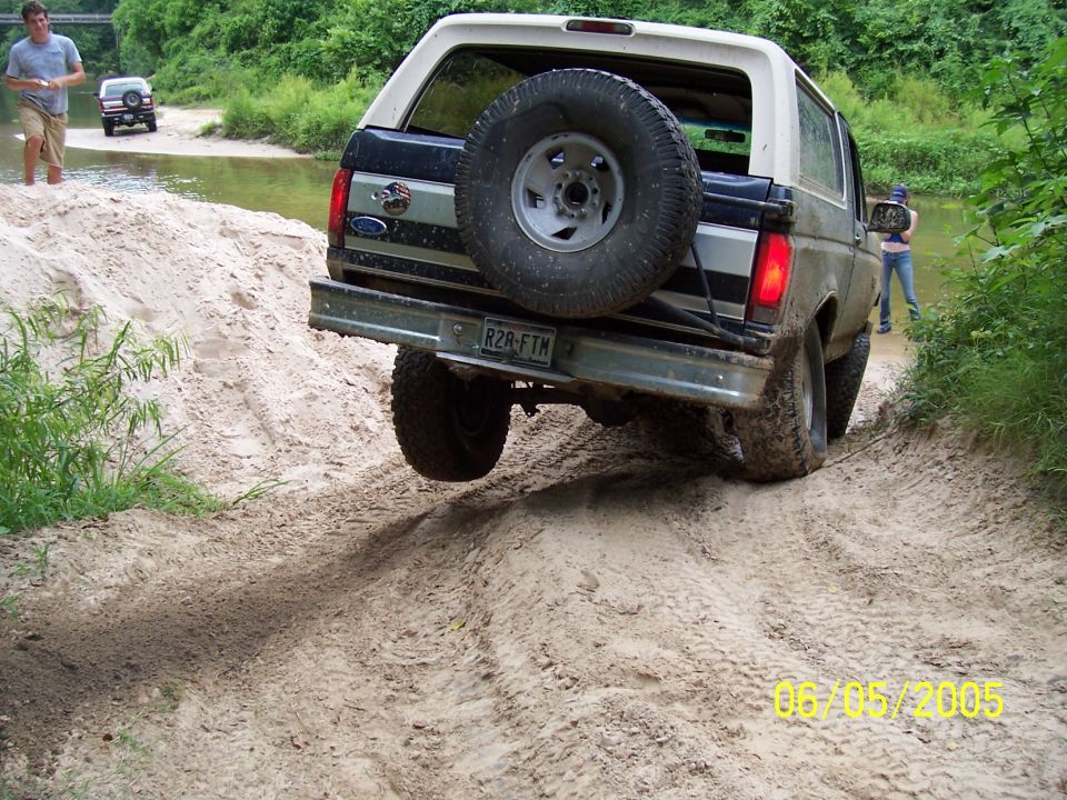 Ford Bronco on a sandy dirt track, rear view, with a spare tire mounted on the back