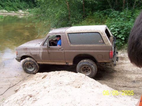 1987 Ford Bronco - 1987 Ford Bronco navigating a muddy off-road trail next to a body of water.