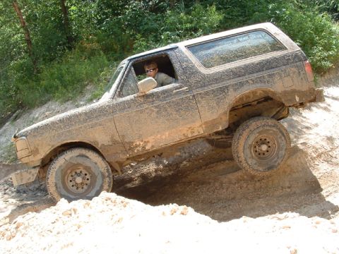 1993 Ford Bronco - This SUV is covered in mud while navigating a challenging off-road terrain.