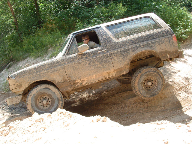 Muddy Ford Bronco flexing through a sand pit off-road, driver at the wheel