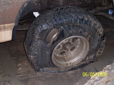 1987 Ford Bronco - A severely damaged tire and wheel, caked in mud, sits in a muddy environment.