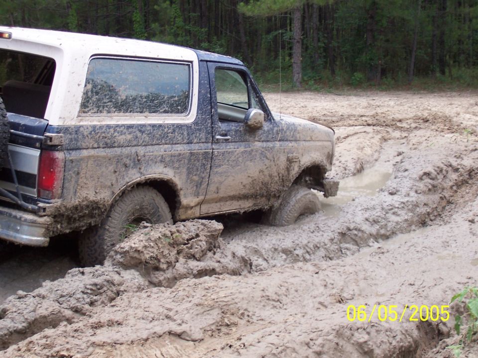 Muddy 1987 Ford Bronco stuck in a mud pit on a wooded trail