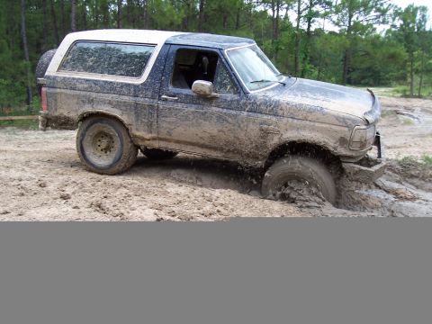 1987 Ford Bronco - This SUV is deeply stuck in thick mud, with its front right wheel almost completely submerged.