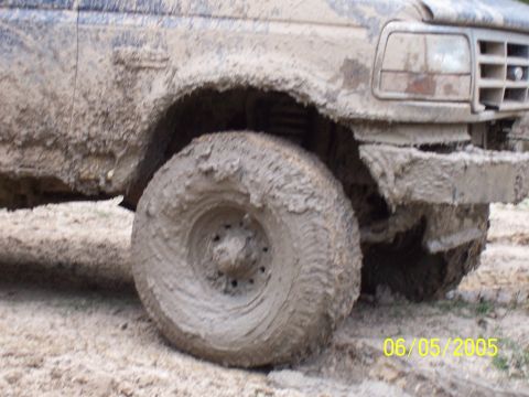 1987 Ford Bronco - This heavily mud-caked truck shows off its off-road capabilities, with the front wheel and fender prominently displayed.