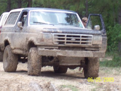 1987 Ford Bronco - Muddy 1987 Ford Bronco on a dirt road with trees in the background.