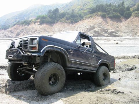 1985 Ford Bronco - Modified Ford Bronco with large tires navigating a muddy terrain.