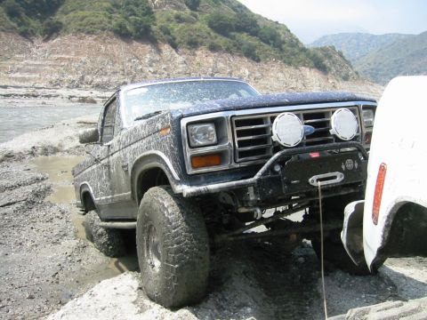 1985 Ford Bronco - Muddy Ford Bronco with aftermarket bumper and winch is stuck in a riverbed.