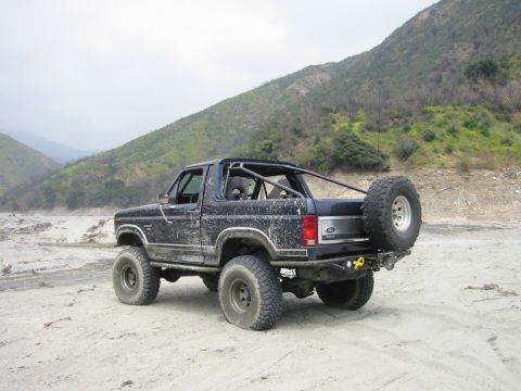 1985 Ford Bronco - Modified 1985 Ford Bronco sits in a dry riverbed with a roll cage and external spare tire.