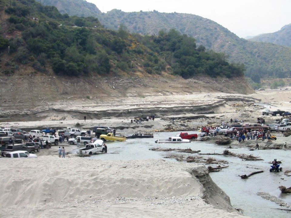 Sandy canyon riverbed crowded with off-road trucks, SUVs, and people
