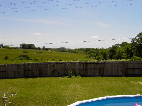 1991 Ford Bronco - A view of a backyard on a sunny day, a fence, lawn, and pool with distant landscape.