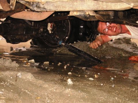 1985 Ford Bronco - A person works on the underside of a 1985 Ford Bronco, showing the driveshaft and transmission.