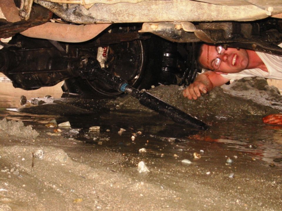 Man lying in mud under a vehicle working on the front axle and undercarriage