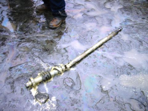 1985 Ford Bronco - A disassembled steering component rests on a wet surface, reflecting iridescent colors from oil.