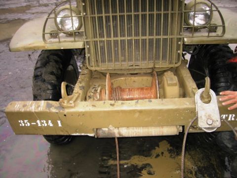 1985 Ford Bronco - A muddy, olive drab truck with a front-mounted winch is partially submerged in water.