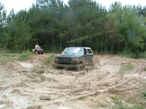 1993 Ford Bronco - A Ford Bronco navigates a muddy off-road course with an ATV in the background.