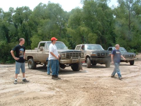 1993 Ford Bronco - A muddy 1993 Ford Bronco is parked with other trucks and people on a dirt lot.