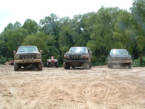 1993 Ford Bronco - Three trucks and two ATVs are parked on a dirt track, with trees in the background.