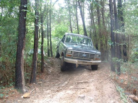 1993 Ford Bronco - A Ford Bronco navigates a challenging muddy path through a dense forest.