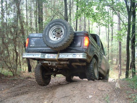 1993 Ford Bronco - This black Ford Bronco is seen from the rear as it navigates a muddy trail through a wooded area.