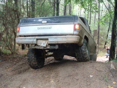 1993 Ford Bronco - This lifted Chevrolet pickup truck is navigating a challenging muddy terrain in a wooded area.
