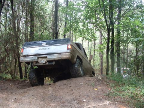 1993 Ford Bronco - A lifted Chevrolet pickup truck navigates a muddy incline in a wooded area.