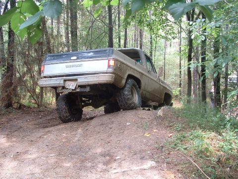 1993 Ford Bronco - A lifted Chevrolet pickup truck navigates a muddy trail through a wooded area.